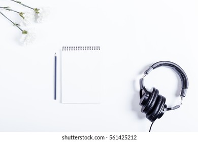 On white table lay notebook, pencil, headphones and flowers, top view
