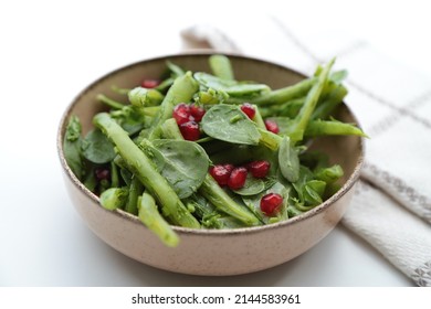 On the white table, pomegranate is added to the purslane and green bean salad in a bowl. It is a local salad of Turkish cuisine. - Shutterstock ID 2144583961