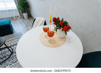 On the white table, there are two glasses of red wine and a beautiful vase filled with colorful flowers, creating a lovely centerpiece that enhances the rooms atmosphere and decor