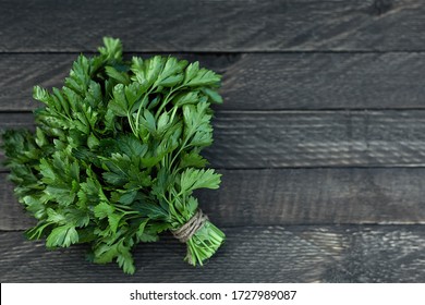 On a wooden background is a bunch of green fresh fragrant parsley.