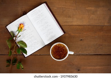 On a wooden background, an open book, next to a rose and a cup of coffee.