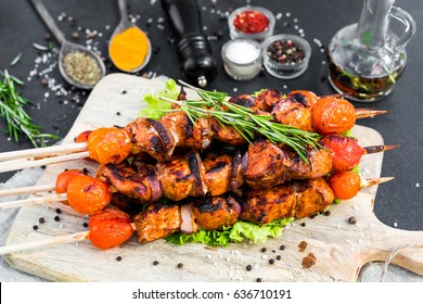 On a wooden board chicken shish kebab, barbecue, grill, black pepper, rosemary, on the background of spices in glass bowls, in wooden spoons,  a bottle of olive oil, black pepper mill, fashion food
