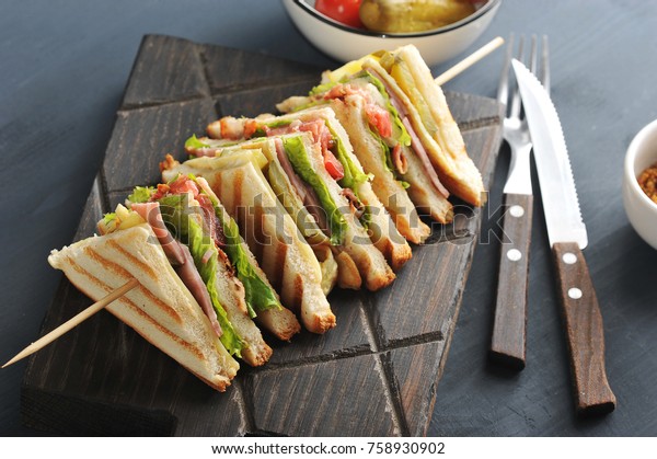 On a wooden\
board a sandwich of white bread. The sandwich is divided into four\
parts and fixed on a wooden skewer. There are cutlery nearby. Dark\
wooden background. Close-up.