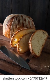 On A Wooden Box Lies Half A Loaf Of Homemade Bread And Sliced. Next Is A Knife.