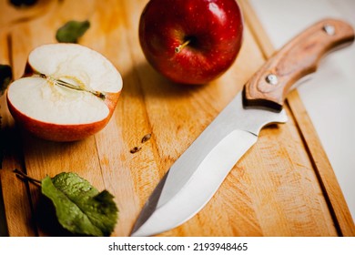 On the wooden kitchen board there is a whole ripe sweet red apple and half an apple, and next to it a sharp kitchen knife. Fruit harvest. Healthy nutrition and vegetarianism.