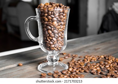 On the wooden table is a glass cup with coffee beans. Coffee beans on a wooden bar counter.