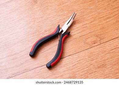 On the wooden table rests a set of pliers, a versatile hand tool commonly used for gripping, bending, or cutting materials. It serves various functions in woodworking and metalworking - Powered by Shutterstock