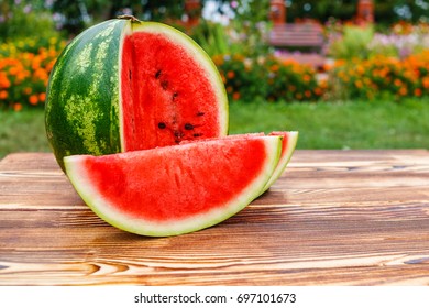 On the wooden table round sliced green striped glossy ripe watermelon with juicy red flesh on open air.  - Powered by Shutterstock