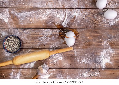 On a wooden table, sprinkled with flour, lie a rolling pin, chicken eggs. An egg broken in the middle of the table.
