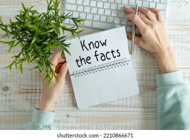On a wooden table there is an office sheet of paper with the text KNOW THE FACTS. Business workspace with calculator, glasses, pen, crumpled paper