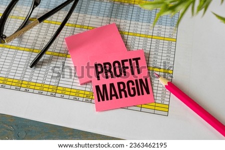 On a wooden table there is an office sheet of paper with the text PROFIT MARGIN. Business workspace with calculator, glasses, pen, crumpled paper and cup of coffee.