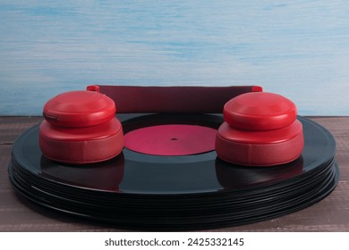 on a wooden table there is a stack of vinyl records , black , and red headphones