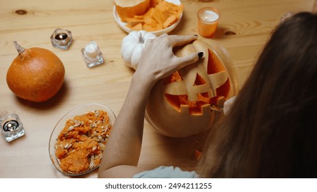 On a Wooden Table in Warm Tones of a Cozy Home Setting, a Woman Carves a Jack-O'-Lantern from a Pumpkin. Candles and Pumpkin Insides on the Table, View from Behind and Above. - Powered by Shutterstock