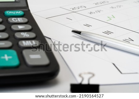 On the working desk are a calculator,  pen, prints with printed calc sheet.  Close up view finance concept

