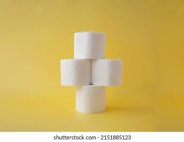 On A Yellow Background, Four Rolls Of Toilet Paper Stand On Top Of Each Other