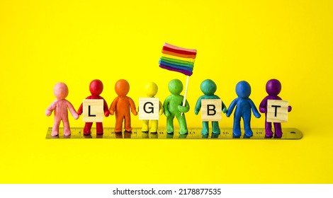 On A Yellow Background, Multi-colored People From Plasticine Stand In A Row On Rulers With Wooden Cubes In Their Hands With The Inscription Lgbt And The Flag Of Gender Equality, A Symbol Of Freedom.