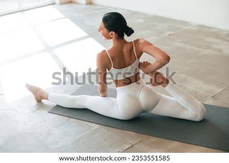 On the yoga mat, practicing. Young woman with slim body type is in fitness clothes in the studio.