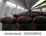 Onboarding preparation in an airplane cabin featuring reclining, comfortable brown seats with red accents and adjustable headrests.