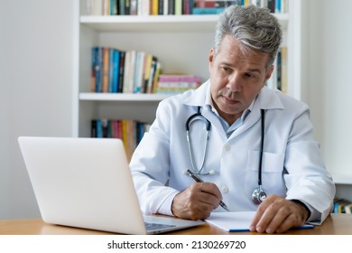 Oncologist Reading Studes About Cancer And Working At Computer At Office Of Hospital