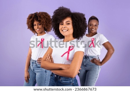 Oncology Awareness Month. Group Of Three Black Ladies With Breast Cancer Ribbons On T Shirts Posing Together In Studio Over Purple Background, Looking At Camera. Selective Focus