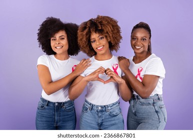 Oncology Awareness. Trio Of Positive African American Ladies With Pink Breast Cancer Ribbons Hugging, Woman Shaping Fingers Like Heart Over Purple Studio Background. Female Support Group - Powered by Shutterstock