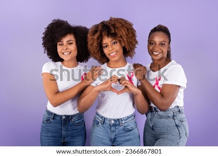 Oncology Awareness. Trio Of Positive African American Ladies With Pink Breast Cancer Ribbons Hugging, Woman Shaping Fingers Like Heart Over Purple Studio Background. Female Support Group