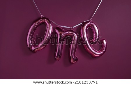 One 1 word metallic balloon on the purple wall background. Party decoration balloons. Anniversary sign for happy holiday, celebration, birthday, carnival, new year, date