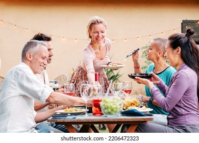 One Adult Blonde Woman Smiling And Serving Plate With Salad On Table, Diverse Friends Sitting Around And Having Fun. Lifestyle Concept. High Quality Photo