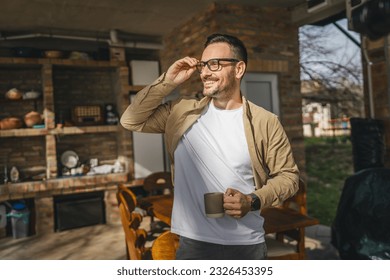 One adult caucasian man stand outdoor in front of his house in sunny morning or day enjoy cup of tea or coffee real people daily routine happy smile copy space - Powered by Shutterstock