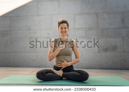 One adult caucasian woman doing yoga meditation practice in summer day outdoor in the city in front of the wall with shadow and sun healthy lifestyle wellbeing concept self care