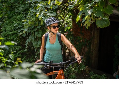 One Adult Caucasian Woman Hold Prepare To Ride Electric E-bike Bicycle In Sunny Summer Day Getting Ready In Front Of The Green Bush Tree Wear Protective Helmet And Eyeglasses Real People Copy Space