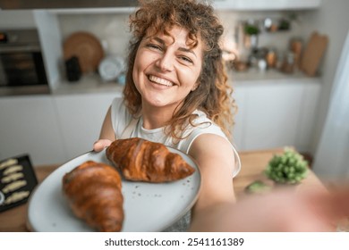 One adult caucasian woman stand in the kitchen with fresh croissant for breakfast daily morning routine - Powered by Shutterstock