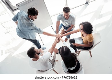 One For All And All For One. Top View On Millennial People Joining Their Hands Together While Sitting In A Circle During An Office Meeting.