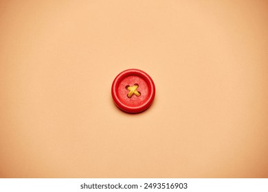 One alone red clothes sewing button with a yellow rope cross isolated on the bright solid fond plain sandy beige background