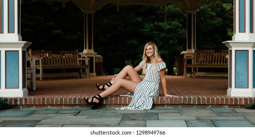 One Attractive Blonde Hair Caucasian High School Senior Posing For Senior Pictures. Female Teenager Portrait Outdoors At Park In Summer.