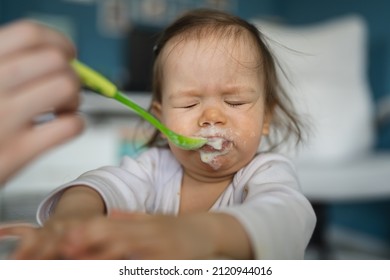 One Baby Close Up On Small Caucasian Girl And Hand Of Her Unknown Mother Feeding Her At Home In Day Small Child With Food Around Mouth Making Mess Dirty While Eating Real People Growing Up Copy Space