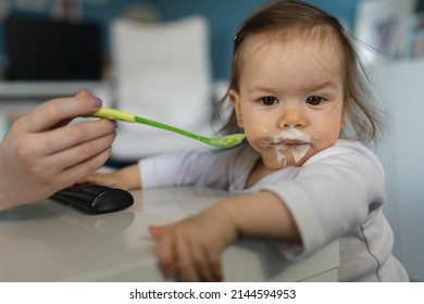 One Baby Close Up On Small Caucasian Girl And Hand Of Her Unknown Mother Feeding Her At Home In Day Small Child With Food Around Mouth Making Mess Dirty While Eating Real People Growing Up Copy Space