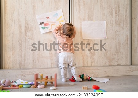 One baby girl back view full length of one infant child standing putting drawing on the wall at home real people copy space family childhood development and growing up concept