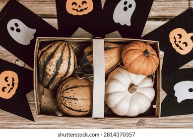 One basket with assorted squashes and a decorative felt black garland with white ghosts and orange pumpkins lies on a wooden table at home on an autumn day, flat lay very close-up. Happy Halloween concept, time to celebrate.