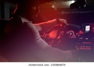 One Bearded Strong Young Man In White Shirt Sitting In Luxury Sport Muscle Car Lit With Red Light In Underground Garage