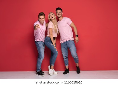 One beautiful blonde woman standing with two handsome men, smiling. Red studio background.