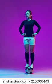 One Beautiful Girl, Professional Female Soccer Player Standing On Football Ball Isolated On Purple Background In Neon. Concept Of Sport, Fitness. Young Spotive Girl In Black And White Football Kit