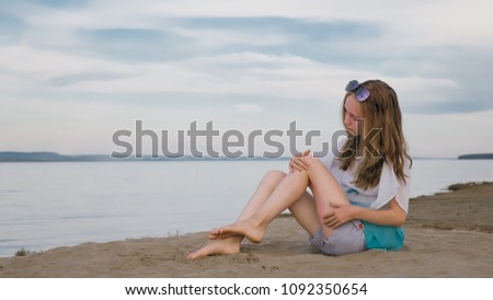 One beautiful teenage girl with brown hair outside on a beautiful summer day. A girl is doing herself a foot massage. Rubbing cream from sunburn. Sunburns are visible on the feet.