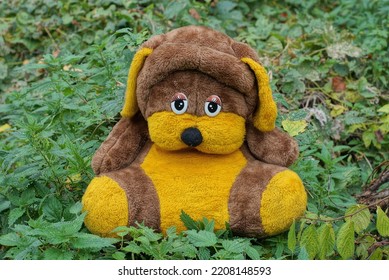 One Big Brown Yellow Plush Toy Dog Sits In Green Vegetation In Nature