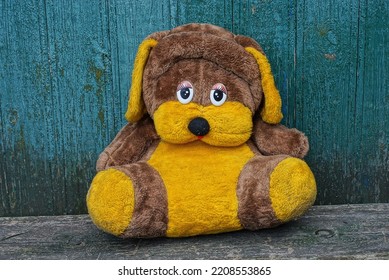 One Big Brown Yellow Plush Toy Dog Sits On A Gray Table Against A Green Wooden Wall