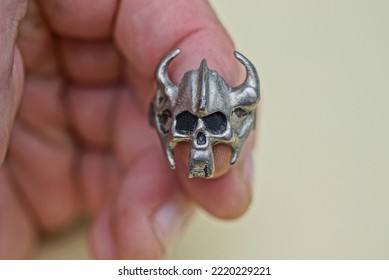 one big gray silver ring in the shape of a skull in a helmet with horns worn on a finger on a hand on a brown background