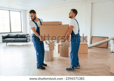 One big heavy box. Two moving service employees in a room.