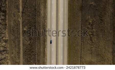 One black car driving alone, lifestyle travel on empty straight asphalt road freeway through empty arid steppe plain at summer sunny day. Aerial drone wide into the distance view.