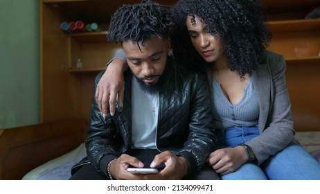 One Black Couple Looking At Cellphone Together In Bedroom