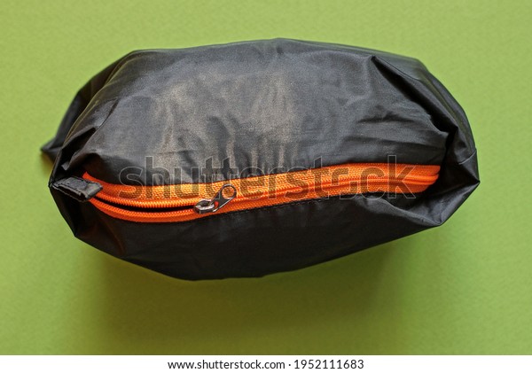 one black full cloth bag with an orange zip stands\
on a green table